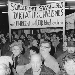 Demonstrierende mit großem Transparent mit dem Text "Schluss mit Stasi u. SED-Diktatur u. Nazismus. Viel Unrecht und Leid klagt euch an"