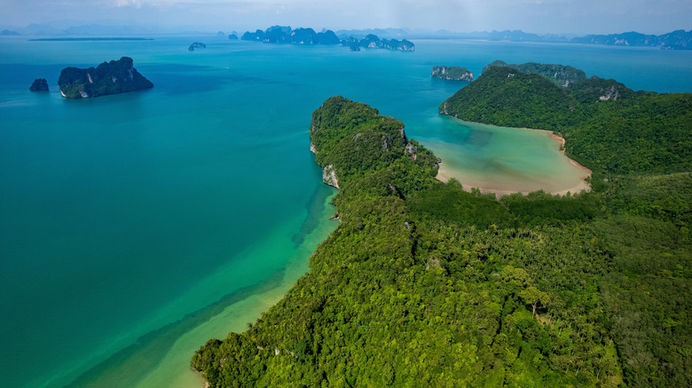 A lush island forming a bay that opens up to open waters, with a smattering of islands in the backdrop