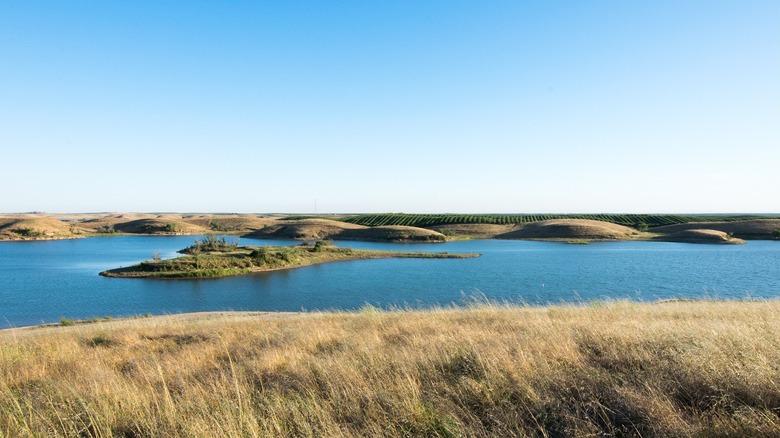 The calm water of Turlock Lake with grassy fields and shorelines on a blue-sky day.