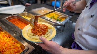 Ein Koch serviert in einer Mensa ein veganes Gericht mit Nudeln und Soja-Bolognese. Laut einer Studie der Uni Konstanz boomt veganes Essen in Hochschulmensen.
