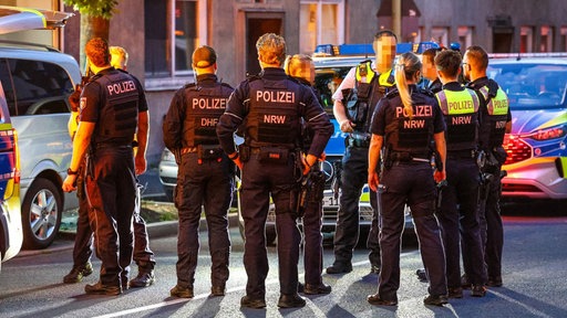 Mehrere Polizisten stehen vor mehreren Dienstfahrzeugen und bereiten einen Einsatz vor