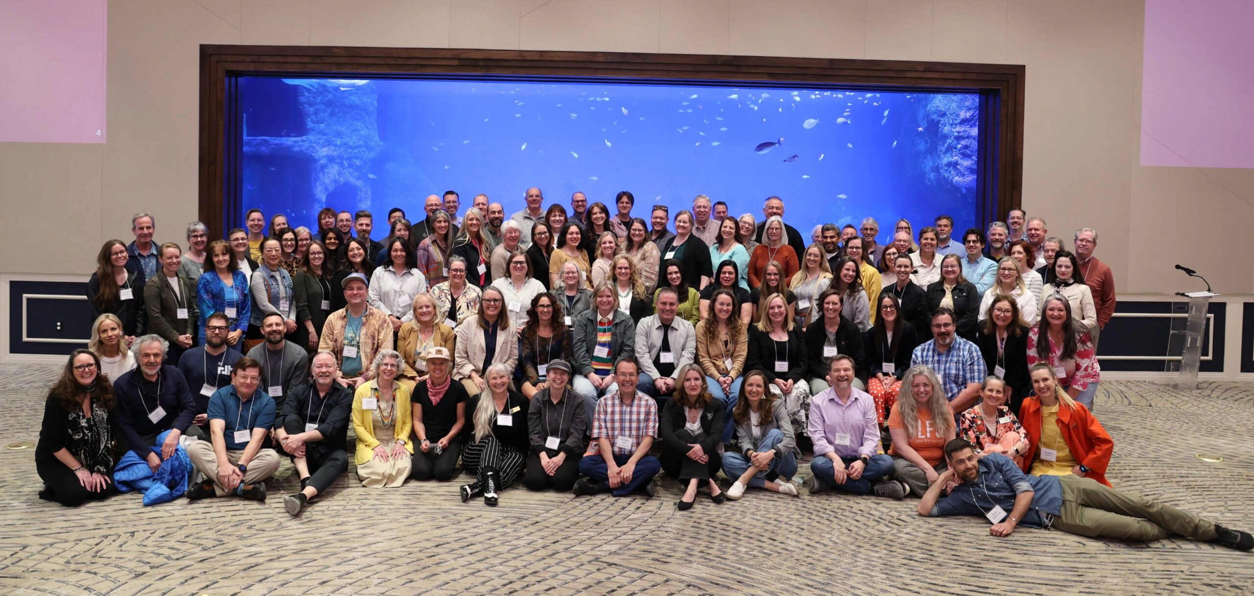 A large group of people posing together in front of a big aquarium tank.