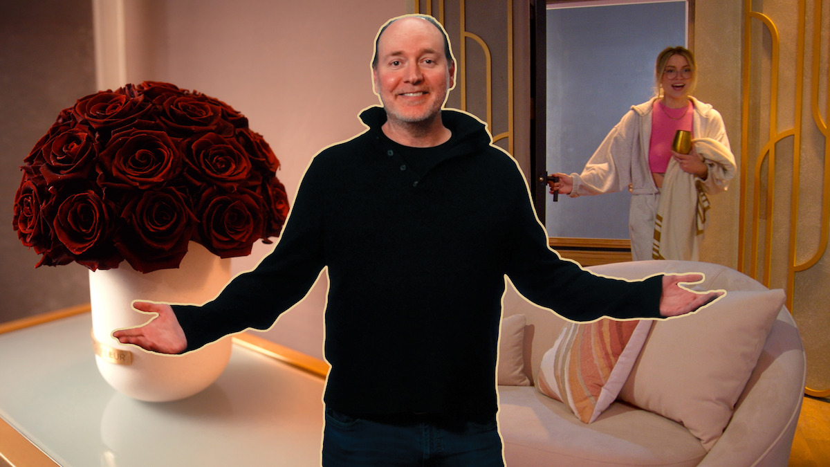 Production Designer Dave Edwards stands with his arms outstretched in front of a pod room. A vase of roses sits on the left, while Madison enters through the door on the right.