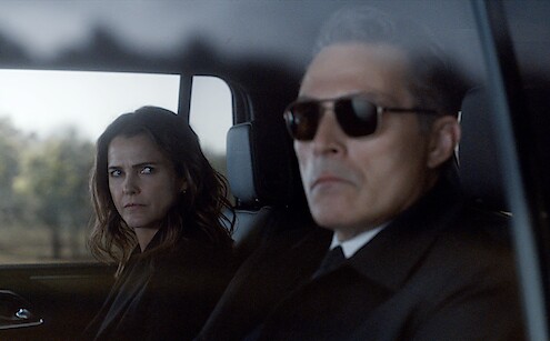 Rufus Sewell as Hal Wyler looks out the window in the back of the car with sunglasses on while Keri Russell as Kate Wyler looks at him suspiciously.