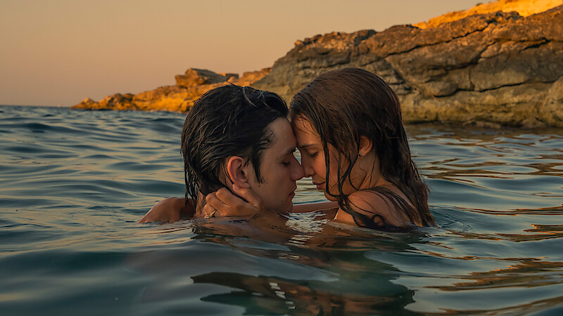 A couple embracing closely in the water near rocky cliffs at sunset, creating a romantic and intimate atmosphere with warm natural lighting.