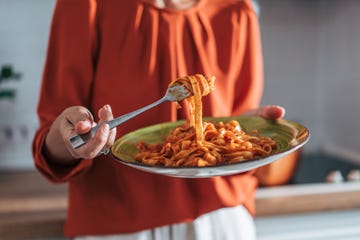 Woman holding plate and fork with tagliatelle and tomato sauce Woman holding plate and fork with tagliatelle and tomato sauce