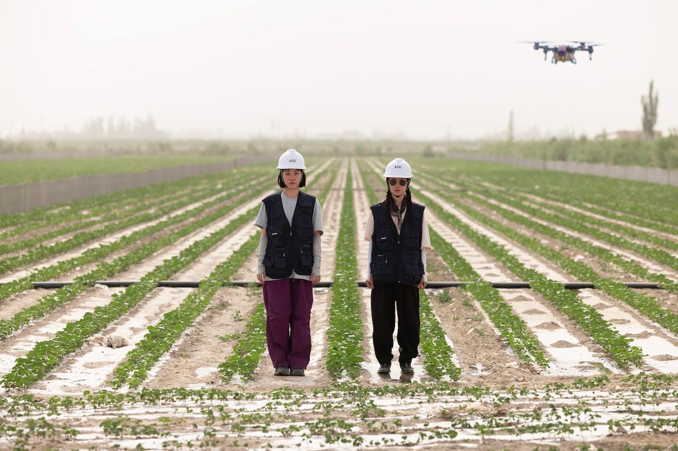 two people in helmets and vests stand in a field with a drone overhead. two people in helmets and vests stand in a field with a drone overhead.