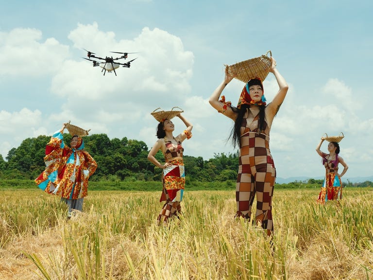 four people in colorful outfits holding baskets in a field with a drone overhead. four people in colorful outfits holding baskets in a field with a drone overhead.