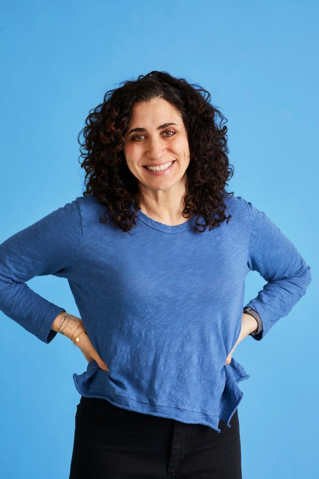 stephanie dolgoff woman with curly hair smiling against a blue background.