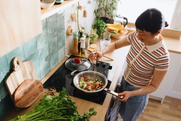 Woman adding spices to vegetables in a frying pan Woman adding spices to vegetables in a frying pan