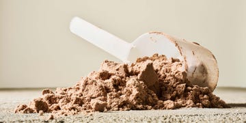 Protein powder spilled with a measuring scoop on a neutral background. Protein powder spilled with a measuring scoop on a neutral background.