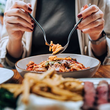 Close-up, mid-section of young Asian woman sitting at dining table holding cutleries, twirling freshly served spaghetti bolognese and enjoying her meal in restaurant. Dining out. People, food and lifestyle woman eating