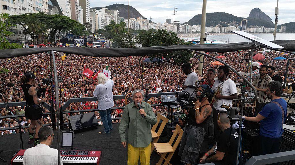 This aerial view shows Brazilian artist Caetano Veloso (C) performing during a protest against the Brazilian Congress to reject a bill that would modify penalties for crimes against democracy and thus reduce the sentence of former president Jair Bolsonaro, at Copacabana Beach in Rio de Janeiro, Brazil on December 14, 2025.