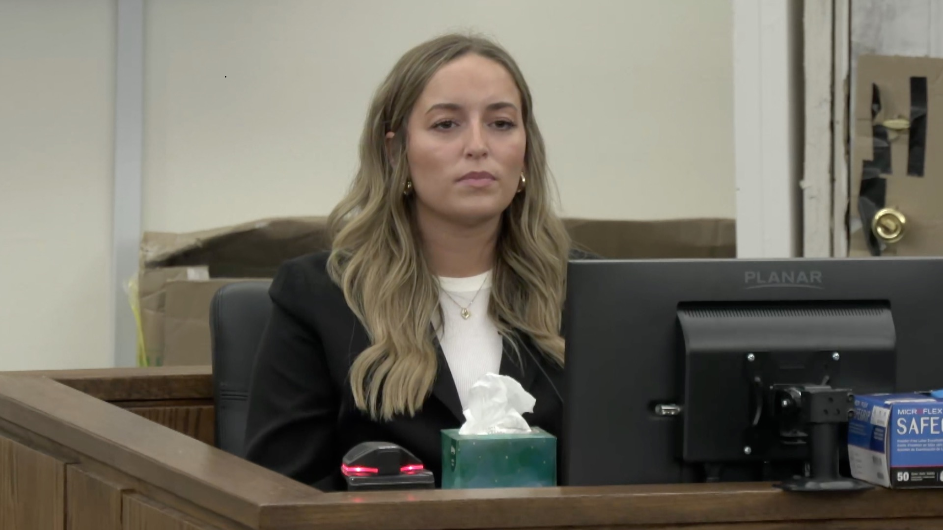 Alleigha Botner testifies in court. She sits before a computer monitor and wears a black jacket, white shirt and shiny necklace and earrings
