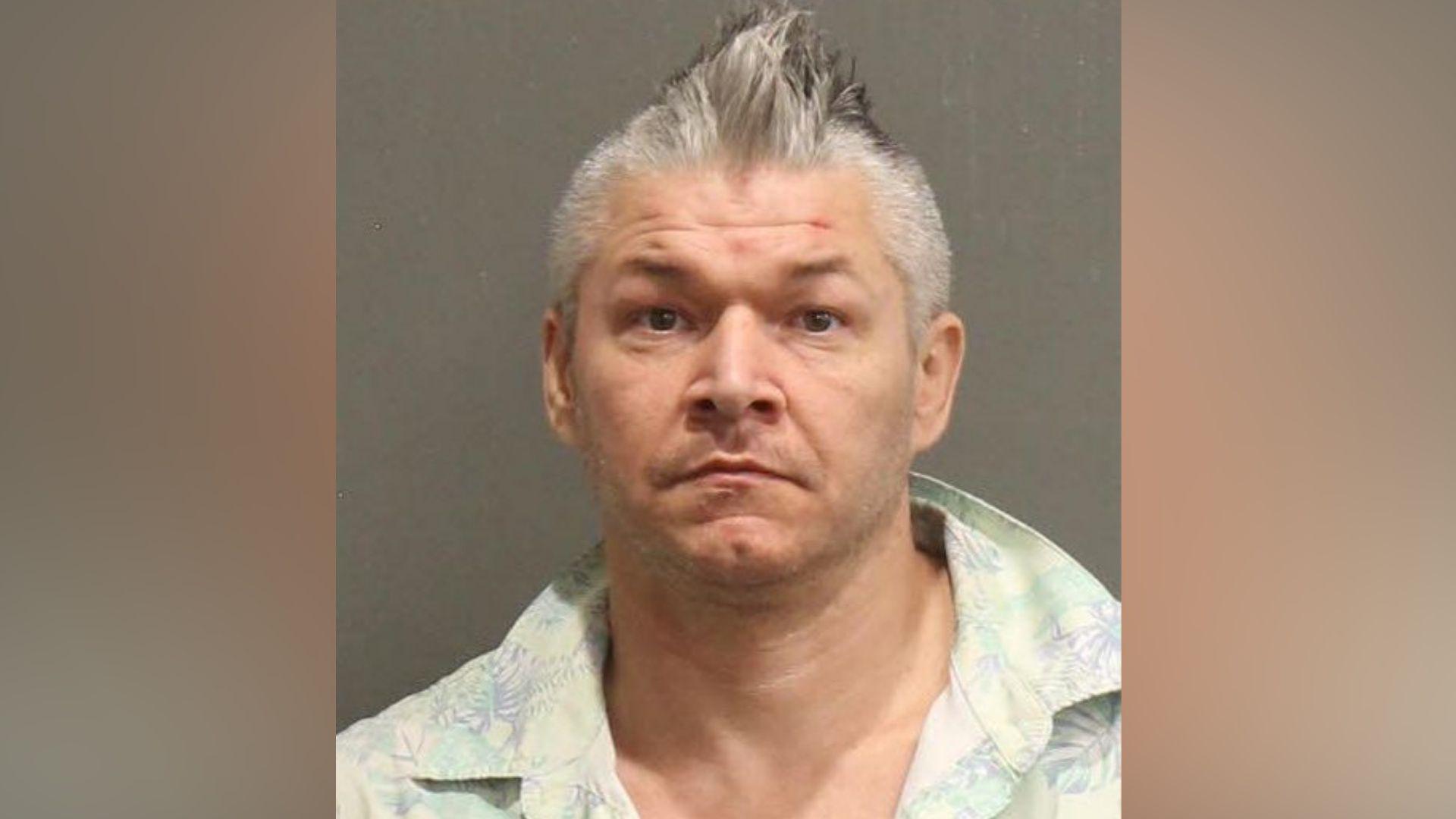 Joseph Rainey, who has grey, spikey hair and is wearing a pastel-coloured, open-collar shirt, in a police mugshot.