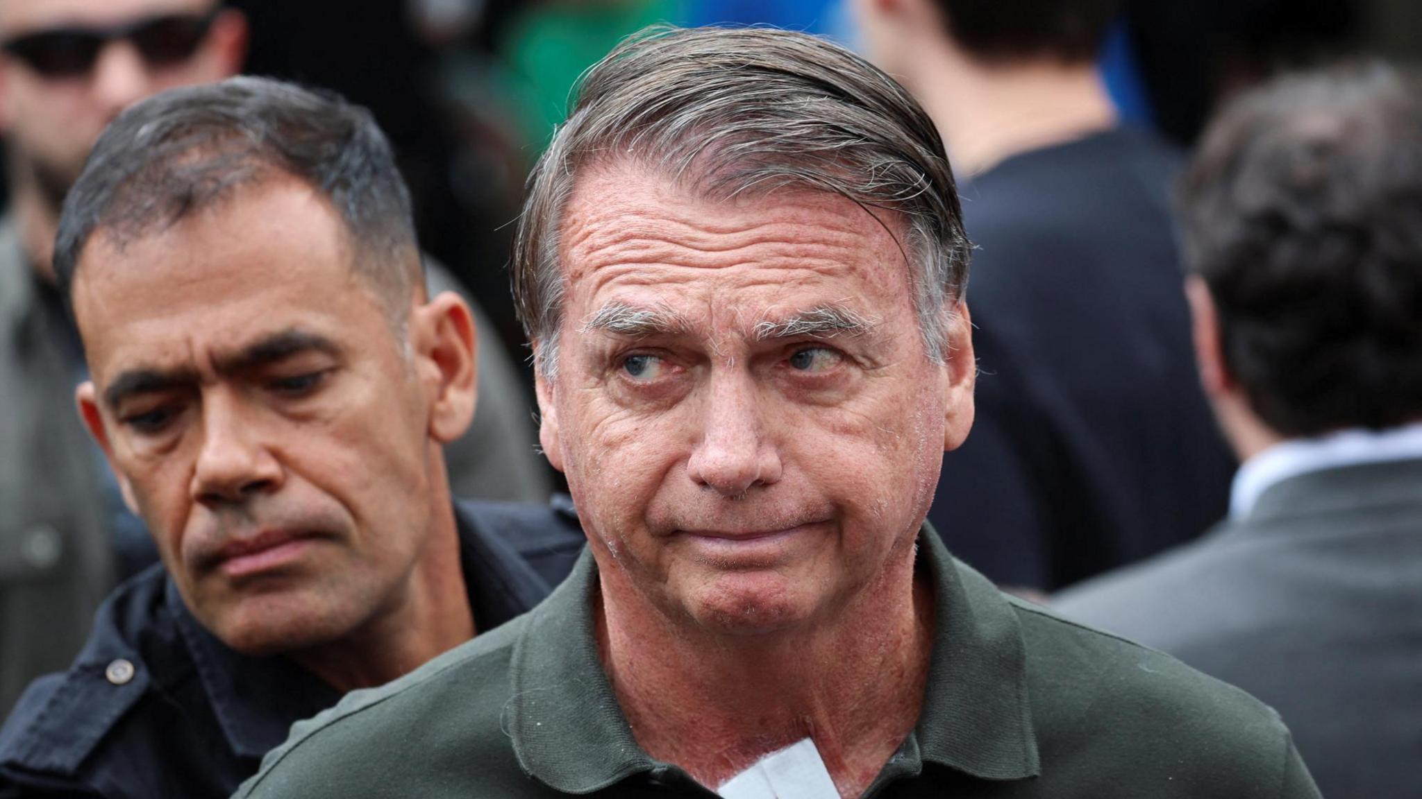 Former Brazilian President Jair Bolsonaro wearing green polo shirt with police officer standing behind him