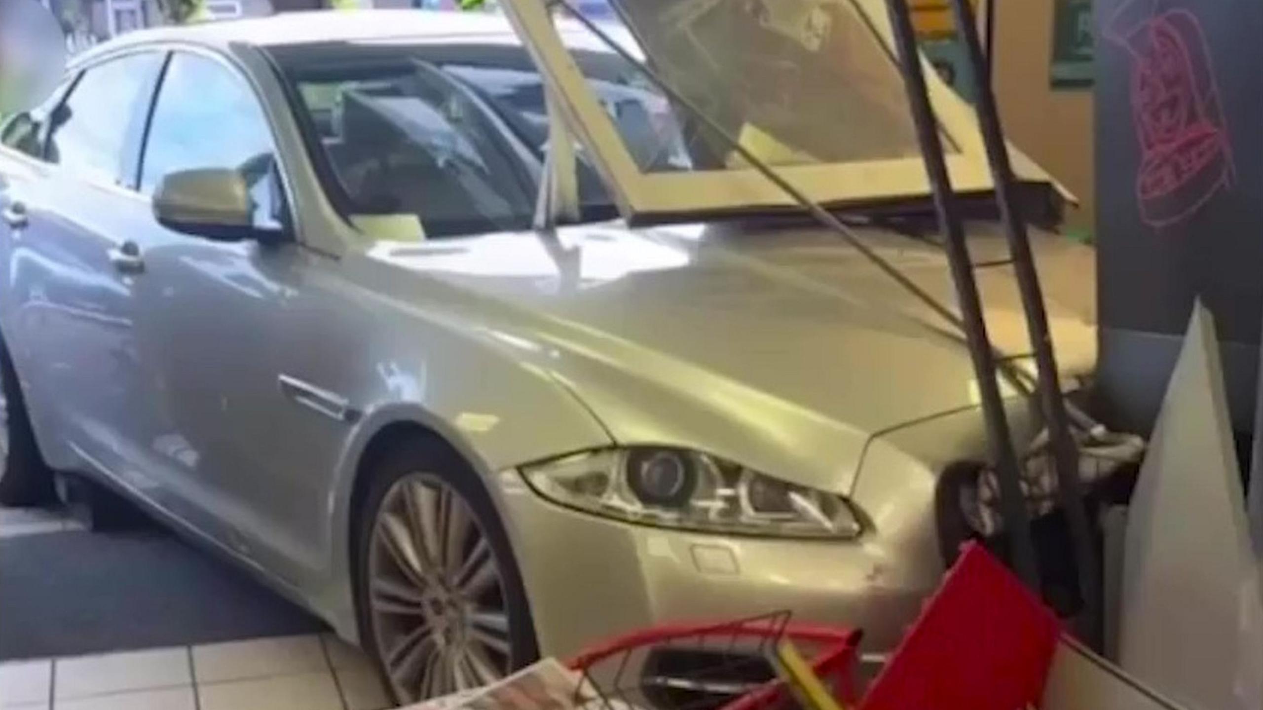 A silver jaguar is pictured after smashing through the front doors of a shop and crashing into a coffee machine with debris around it