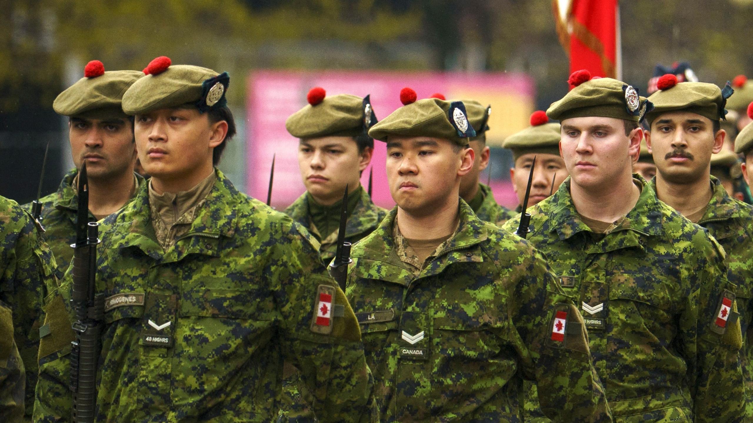 Canadian troops wearing green camouflage and wearing berets march