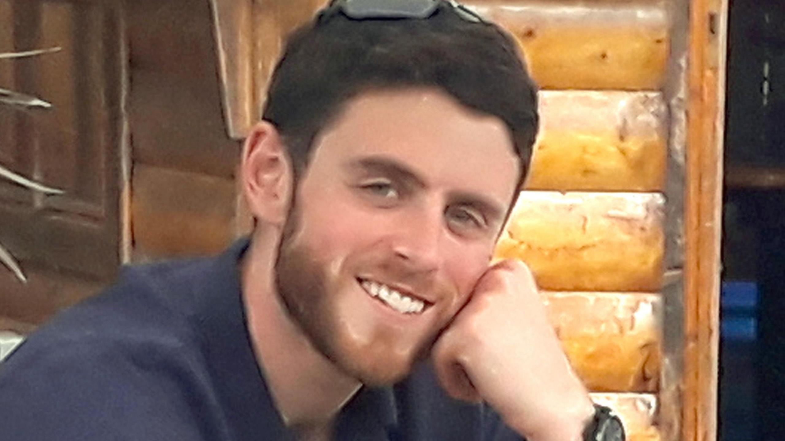 A young man poses with his face resting on his hand in a casual manner