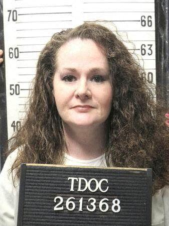 Christa Pike has long auburn hair. She is standing in front of a height chart and holding up a sign with an identifying number.