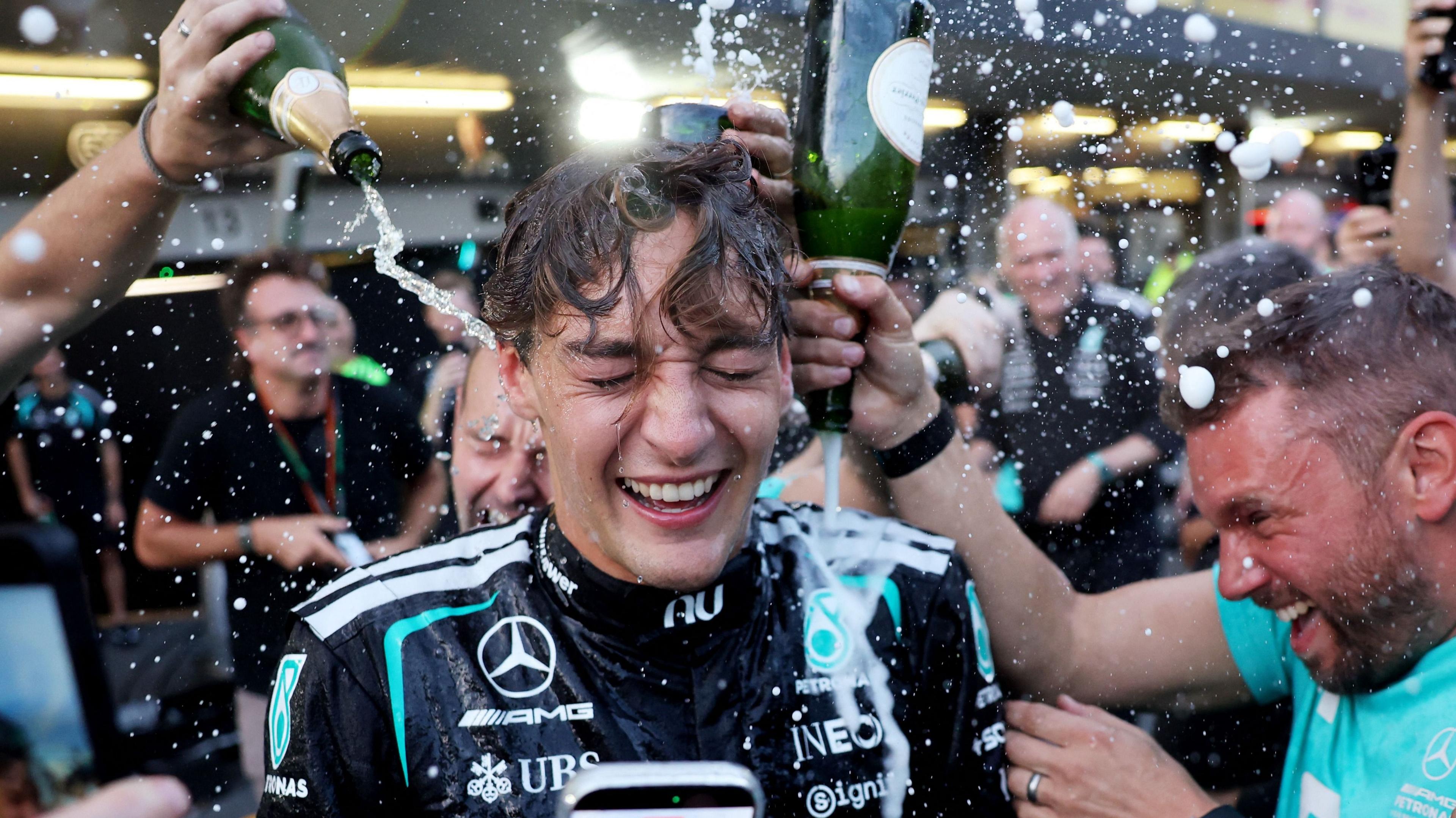 George Russell celebrating with Mercedes team members pouring champagne over him