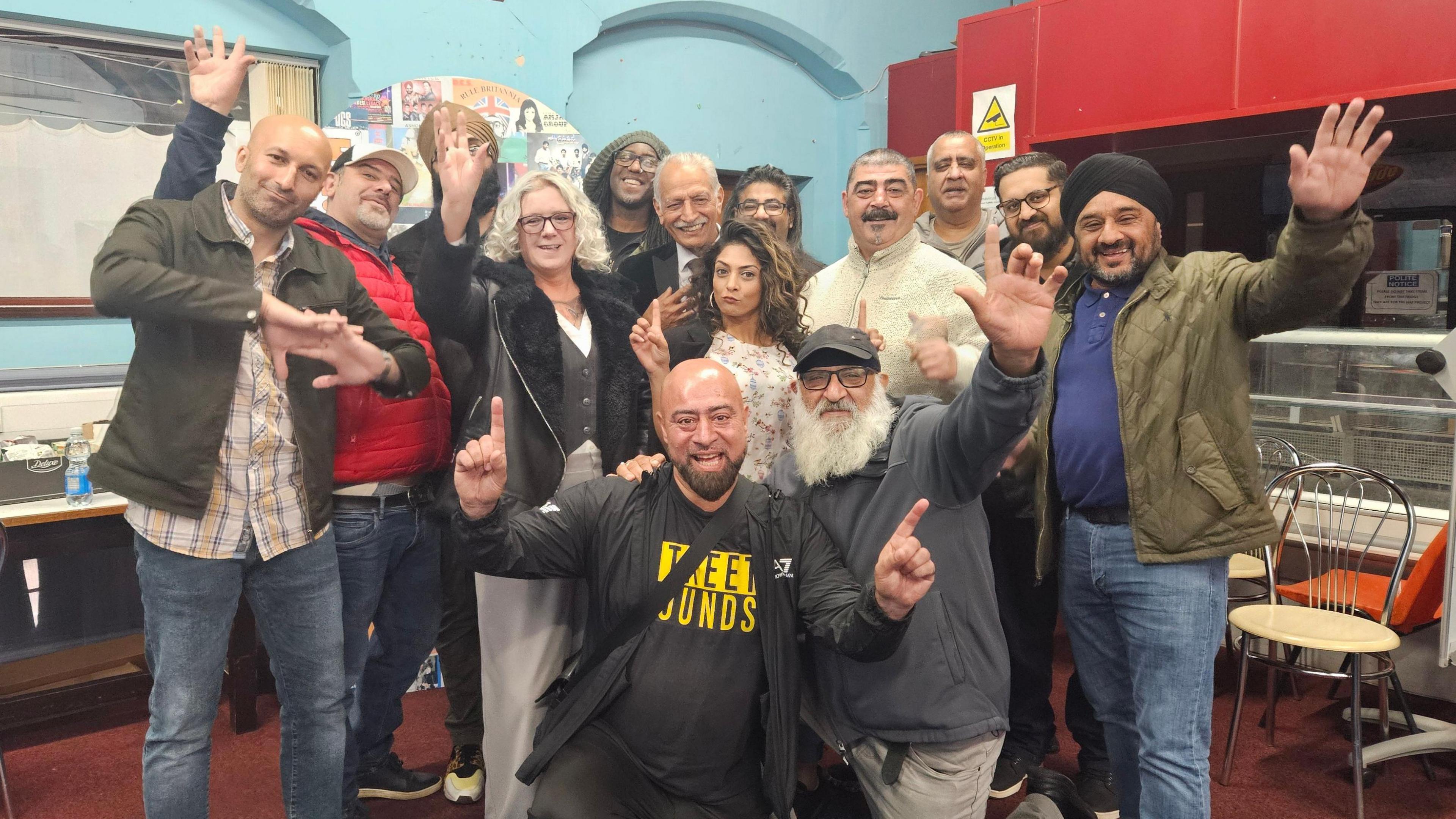 A group of people posing happily, some of them with their hands in the air in a 'bhangra dance' style
