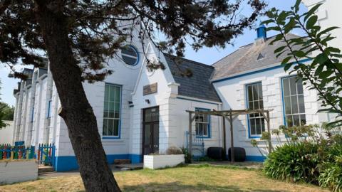 St Christopher's School is a white building with blue trim. It has grass and a tree in front of it.