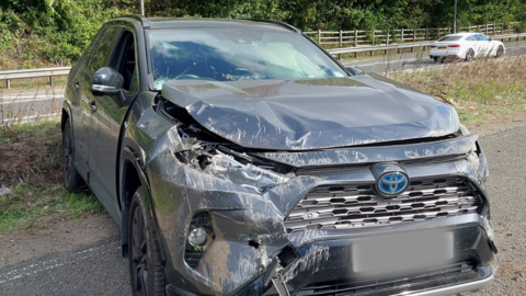 A damaged car parked on a verge by the side of a motorway.