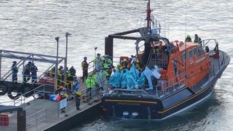People wrapped in blankets on the back of an RNLI lifeboat moored by a pontoon at Eastney, Portsmouth, on 6.9.26