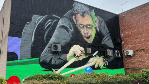 A large painted wall showing a snooker player dressed in black about to take a shot on the table