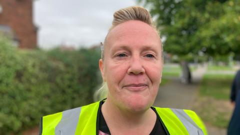 Joanne, a woman with blonde hair. She is wearing a green and grey High-visibility sleeveless jacket.