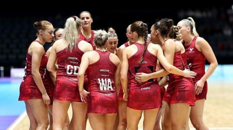 Welsh Feathers players wearing red netball dresses in an on-court huddle