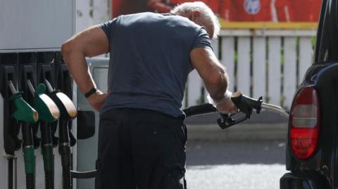 A man in a grey T-shirt and dark shorts fills a vehicle with diesel fuel.