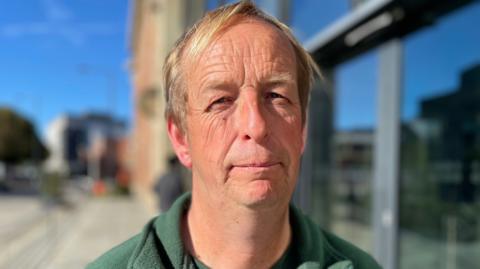 A man with blonde hair wearing a green fleece jumper.