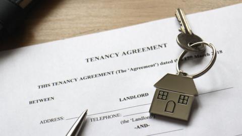 A close up of a contract, with a pen and a key resting on it. The keyring is in the shape of a house, while the paper states TENANCY ARGREEMENT at the top of the paper, with details underneath asking for the name and address of the person signing it.
