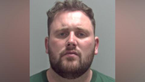A mugshot of Ernest Oakley, who wears a green T-shirt and has a beard.