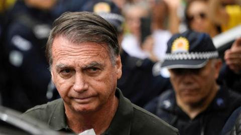 Jair Bolsonaro is wearing a dark green polo short as he leaves hospital on 14 September in Brasilia. A police officer can be seen behind him.