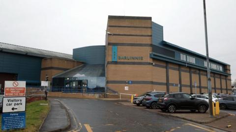 The front entrance to a prison with a Barlinnie sign and cars parked outside