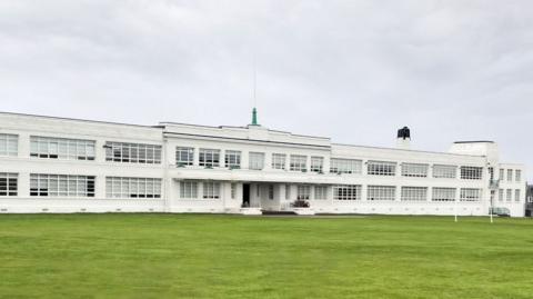 Inverness High School's main building is of a 1930s white walled art deco style with sleek lines, including long windows.