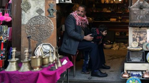 A man wearing a red keffiyeh sits in the doorway of a shop with items of display outside, in a bazaar in Old Cairo (file photo)