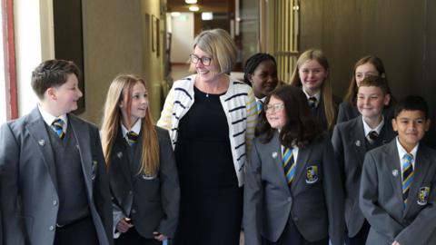A number of pupils in their school confirms flank principal Ruth Harkness in a hallway.