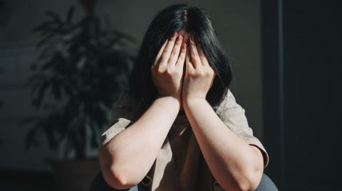A young woman with dark hair with her head in her hands. her face is not visible, just her forearms and her hair