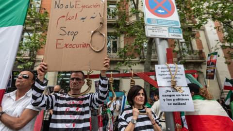Two people dressed as hanged prisoners, with painted blood on their faces and nooses around their necks, take part in a protest against executions in Iran by opponents of the Islamic Republic, outside the US embassy of Madrid, Spain (11 April 2026)