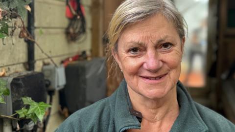 A head and shoulders image of Sue Stubley standing outside while wearing a green sweater. She is smiling and looking into the camera.