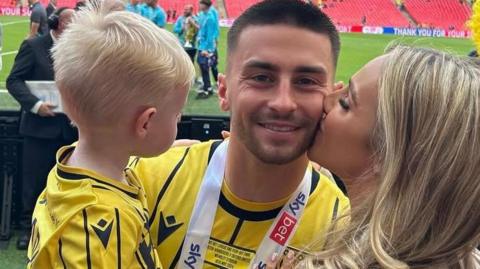 Owen, Jessica and Xavier on the pitch, with Jessica giving Owen a kiss on the cheek