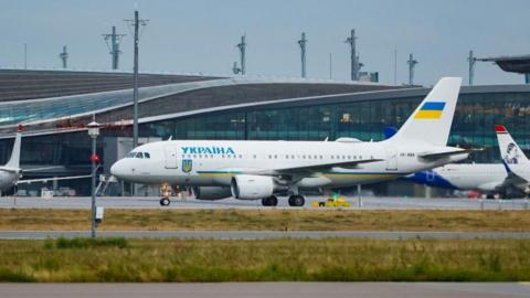 A white painted passenger plane sits on a runway at an airport after landing