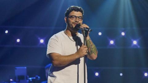 Diogo is singing on a stage for The Voice UK.