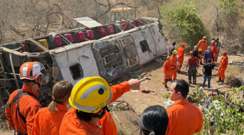 A bus on its side, surrounded by emergency workers wearing orange outfits. Some have hats on.