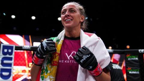 Dakota Ditcheva wearing MMA gloves with a flag draped over her shoulders