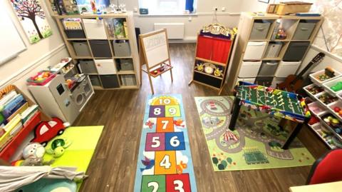 A room with play toys, floor mats, boxes, cases and books.